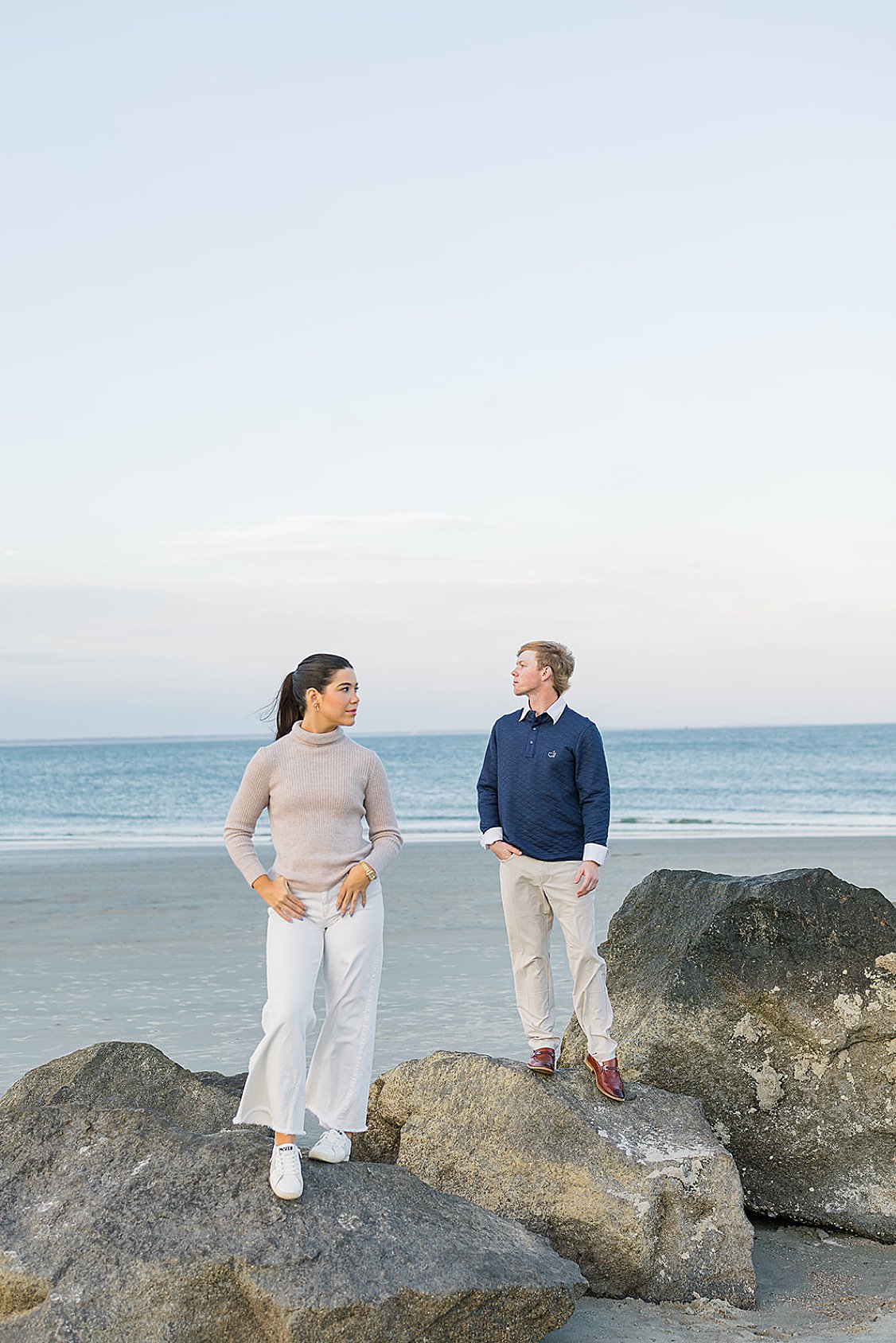 Couple walking hand in hand along Tybee Island beach at sunset, dressed in soft coastal chic attire.