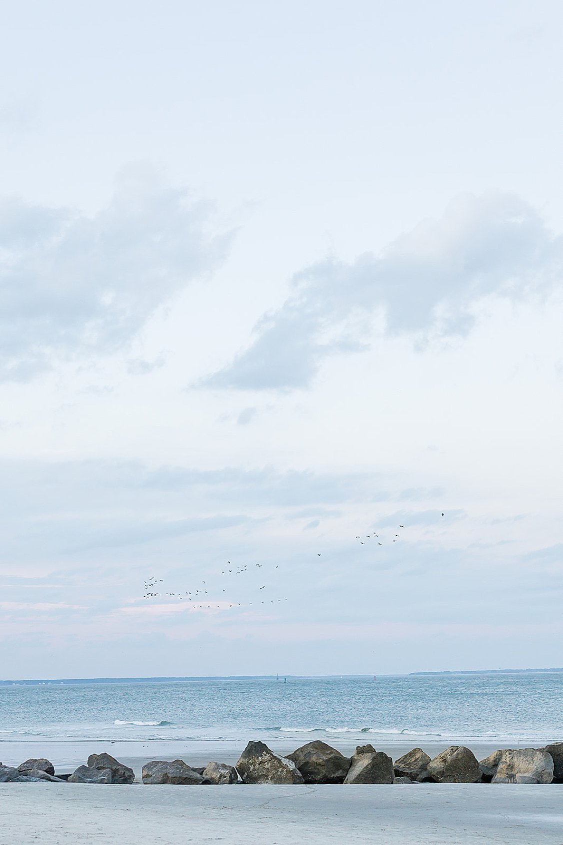 Couple walking hand in hand along Tybee Island beach at sunset, dressed in soft coastal chic attire.