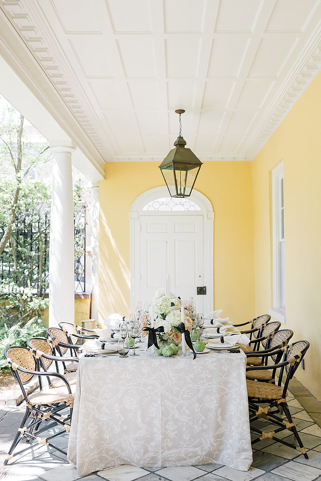 Historic yellow William Aiken House in Charleston surrounded by lush greenery and neutral floral accents.