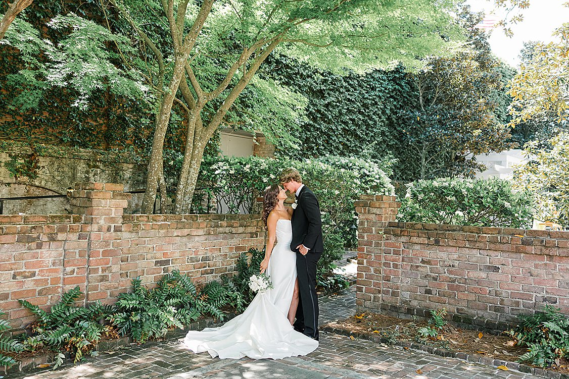 Editorial groom styling in classic attire surrounded by natural greenery and yellow Charleston architecture.